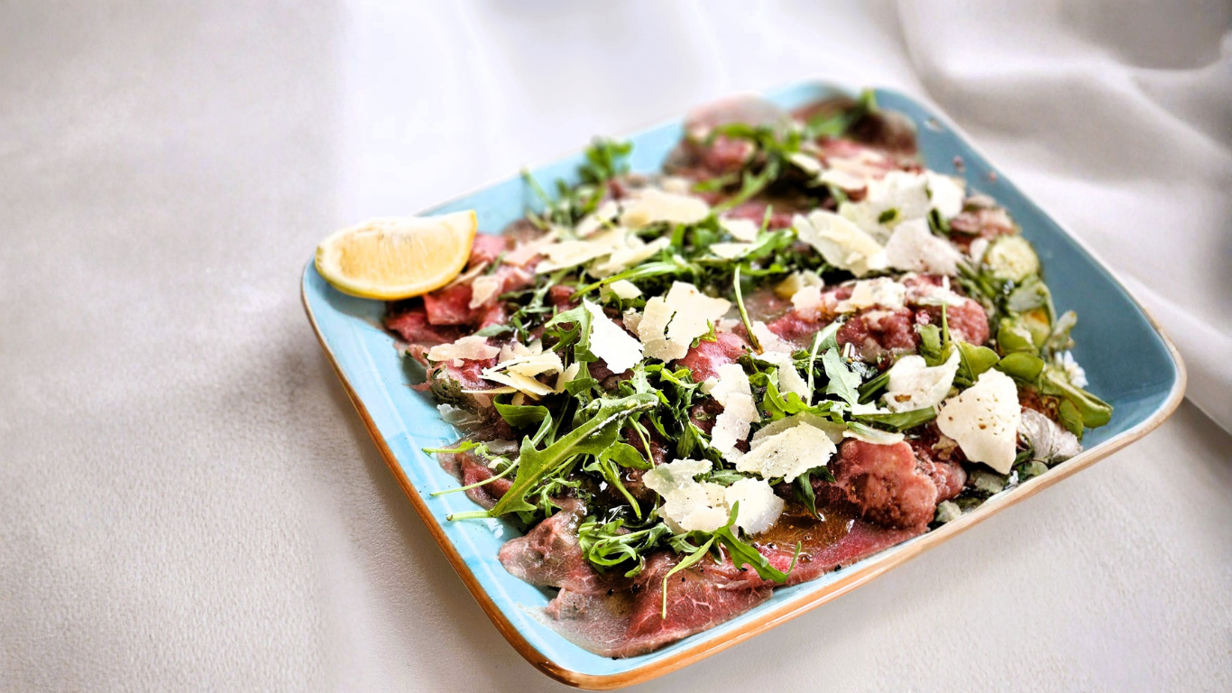 Salat mit Rindfleisch, Rucola, Feta und Zitronenscheibe auf einem blauen Teller.